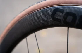 Primer plano de una rueda de bicicleta que muestra un neumático de flanco marrón montado en una llanta negra de fibra de carbono con radios visibles, destacando el rendimiento y la ligereza de las Ruedas Corima 45R.