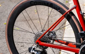 Primer plano de la rueda trasera y el sistema de cambios de una bicicleta de carretera roja con Ruedas Corima 45R, aparcada en una calle asfaltada cerca de un bordillo, destacando la ligereza y el rendimiento óptimo.