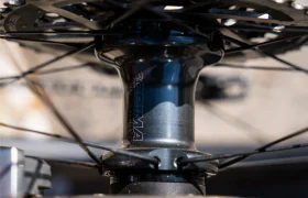 Primer plano de un buje de rueda de bicicleta con radios metálicos y parte de un disco de freno. El buje "PRIMA" destaca el rendimiento y la ligereza, similar a la ingeniería avanzada que se ve en Ruedas Corima.