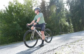 Una persona con casco e indumentaria ciclista monta en una bicicleta equipada con ruedas Corima Essentia 42 por una carretera asfaltada rodeada de árboles y vegetación.