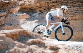 Un ciclista con casco y equipo de ciclismo conduce una bicicleta de carretera blanca con ruedas Zipp 2026 por un camino rocoso e iluminado por el sol, listo para rodar más rápido.