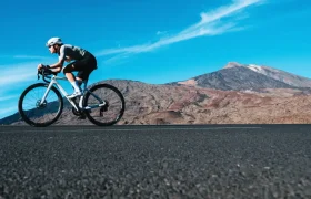 Un ciclista monta una bicicleta de carretera Zipp 2026 en una carretera pavimentada con un paisaje montañoso y un cielo azul, disfrutando de rodar más rápido en el pintoresco telón de fondo.