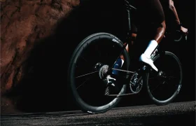 Primer plano de una persona en una bicicleta de carretera por una carretera asfaltada, con la rueda trasera Zipp 2026 avanzada para quienes buscan rodar más rápido. El enfoque se centra en la rueda trasera y la parte inferior del cuerpo del ciclista.