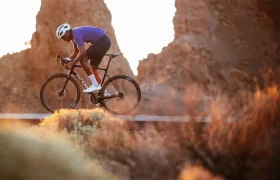 Un ciclista vestido con un maillot azul y un casco blanco circula con una bicicleta de carretera Zipp 2026 por un sendero al aire libre con formaciones rocosas al fondo, listo para rodar más rápido.