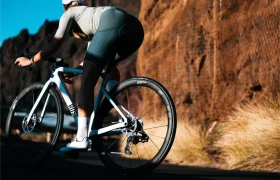 Un ciclista con casco y equipo de ciclismo circula en una bicicleta de carretera blanca equipada con ruedas Zipp 2026 por una carretera asfaltada junto a un acantilado rocoso e iluminado por el sol, dispuesto a rodar más rápido en cada tramo.