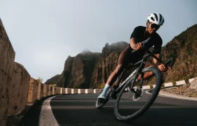 Un ciclista con casco y gafas de sol conduce una bicicleta de carretera Zipp 2026 por una curva en una carretera de montaña con acantilados rocosos al fondo, listo para rodar más rápido.