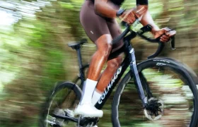 Un ciclista con pantalones cortos oscuros y una camiseta negra monta rápidamente una bicicleta de carretera Zipp 2026 a través de un fondo boscoso y borroso, listo para rodar más rápido gracias a la conectividad inteligente y el rendimiento superior.