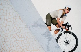 Un ciclista con casco y equipo de ciclismo conduce una bicicleta blanca equipada con ruedas Zipp 2026 junto a una estructura grande, alicatada y angular con un fondo neutro, listo para rodar más rápido.