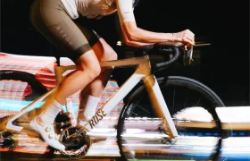 Un ciclista con pantalones cortos marrones y maillot blanco avanza a toda velocidad en la noche sobre una bicicleta Rose blanca con ruedas Zipp 2026, luces borrosas que insinúan rodar más rápido y un rendimiento inigualable.