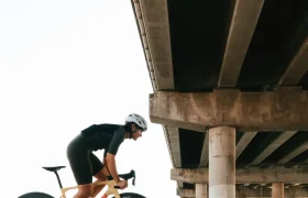 Un ciclista que lleva casco pedalea en una bicicleta de carretera equipada con ruedas Zipp 404 S, deslizándose bajo un gran paso elevado de hormigón con múltiples columnas de soporte, centrado en la velocidad y el rendimiento.