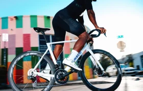 Una persona circula en una bicicleta de carretera blanca con ruedas Zipp 404 S por una calle de la ciudad, pasando junto a un edificio con una fachada colorida y a rayas.