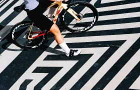 Una persona que lleva casco y equipación de ciclismo posa junto a una bicicleta Zipp 404 S sobre una llamativa superficie con motivos geométricos en blanco y negro, lista para superar los límites de la velocidad.