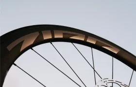 Primer plano de una rueda de bicicleta Zipp 404 S, en el que destacan su elegante llanta, los radios y el freno de disco —todo ello diseñado para la velocidad y el máximo rendimiento—, con un cielo despejado como telón de fondo.