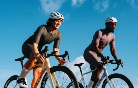 Dos ciclistas, con casco y equipación de ciclismo, pedalean uno al lado del otro en unas elegantes bicicletas de carretera, equipadas con ruedas Zipp 404 S para ganar velocidad, en un día soleado con un cielo azul de fondo.