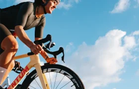 Un ciclista, equipado con casco y ropa de ciclismo, pedalea en una bicicleta amarilla equipada con ruedas Zipp 404 S al aire libre, bajo un cielo azul con nubes dispersas, disfrutando de una mayor velocidad y rendimiento.