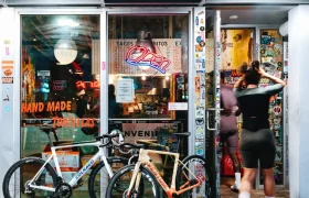 Hay dos bicicletas aparcadas frente a un restaurante bien iluminado con un cartel que dice «Abierto»; una de ellas está equipada con ruedas Zipp 404 S, conocidas por su velocidad; una persona vestida con ropa de ciclista está entrando por la puerta.