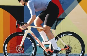 Un ciclista, que lleva casco y gafas de sol, pasa a gran velocidad junto a un colorido mural geométrico montado en una bicicleta de carretera blanca equipada con ruedas Zipp 404 S.