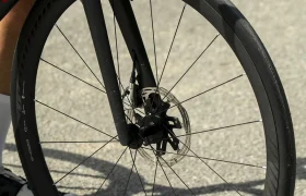 Primer plano de la rueda delantera de una bicicleta de carretera con llanta de carbono Zipp 202 NSW y freno de disco, equipada con un neumático Schwalbe Pro One Aero, colocada sobre una superficie asfaltada.