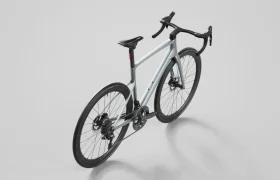 Se muestra una moderna bicicleta de carretera SCOTT Addict con manillar rebajado, frenos de disco y cuadro gris claro sobre un fondo claro liso, vista desde el ángulo lateral trasero.
