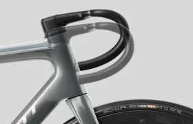 Primer plano de la parte delantera de una bicicleta de carretera SCOTT Addict que muestra el manillar, la horquilla y la rueda delantera con un neumático Schwalbe Pro One sobre un fondo claro liso.