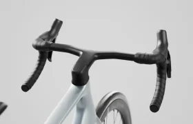Primer plano del manillar y la rueda delantera de una bicicleta SCOTT Addict sobre un fondo liso de color gris claro.