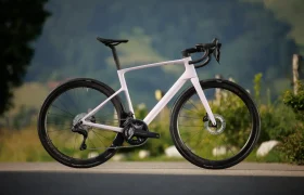 Una moderna bicicleta de carretera SCOTT Addict con cuadro blanco y negro está aparcada en la acera, sobre un fondo natural verde difuminado.