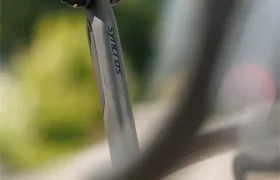 Primer plano de un sillín y una tija de bicicleta con la etiqueta "Syncros" en una SCOTT Addict, con parte de la rueda trasera y un fondo borroso visibles.