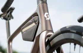 Primer plano de un moderno cuadro de bicicleta de carretera SCOTT Addict con una pequeña bolsa de almacenamiento adjunta, centrándose en el manillar y la rueda delantera, sobre un fondo borroso al aire libre.