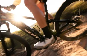 Primer plano de una persona montando una bicicleta de montaña SCOTT Strike 2027 negra por un sendero de tierra, con la luz del sol filtrándose a través del cuadro de la bicicleta y un efecto de movimiento difuminado al fondo. El potente motor Bosch CX garantiza una conducción suave y aporta un confort adicional incluso en terrenos accidentados.