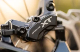 Primer plano de una pinza de freno de disco Shimano Deore XT montada en una bicicleta SCOTT Strike 2027, con parte del disco de freno visible al fondo. Esta configuración, combinada con el motor Bosch CX, garantiza una frenada potente y una mayor comodidad en cada salida.