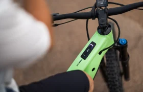 Primer plano de una persona sentada en una bicicleta eléctrica SCOTT Strike 2027 de color verde, en el que se aprecian el indicador de batería y el manillar ergonómico de la bicicleta, junto con parte de la rueda delantera y el potente motor Bosch CX.