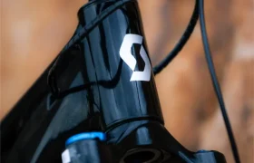 Primer plano de la parte delantera de una bicicleta SCOTT Strike 2027 negra, con los cables a la vista y un logotipo «S» blanco en el cuadro, en el que destaca su motor Bosch CX y su diseño pensado para ofrecer la máxima comodidad, todo ello sobre un fondo marrón difuminado.