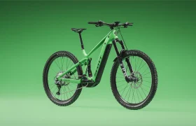 Una bicicleta de montaña verde con suspensión total, como la SCOTT Strike 2027 con motor Bosch CX, ofrece tanto comodidad como rendimiento gracias a sus neumáticos anchos y sus potentes frenos de disco, que resaltan maravillosamente sobre un fondo verde a juego.