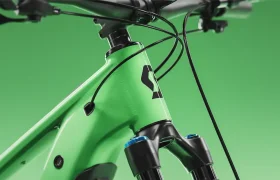 Primer plano de la parte delantera del cuadro de una bicicleta SCOTT Strike 2027 de color verde, en el que se aprecian la horquilla de suspensión, los cables y el logotipo negro, sobre un fondo verde liso. Diseñado para ofrecer un confort óptimo, este modelo cuenta con opciones de integración avanzadas, como el motor Bosch CX.