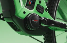 Primer plano de un motor Bosch Performance CX instalado en una bicicleta eléctrica SCOTT Strike 2027 de color verde, en el que se aprecian la biela, la carcasa del motor y parte de la rueda trasera sobre un fondo verde, lo que resalta a la perfección tanto la avanzada tecnología del motor Bosch CX como el mayor confort para el ciclista.
