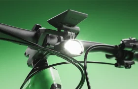 Primer plano del manillar de una bicicleta SCOTT Strike 2027 con un faro delantero encendido y una pantalla digital, sobre un fondo verde, que destaca la comodidad y la avanzada integración del motor Bosch CX.