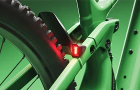 Primer plano del cuadro verde de una bicicleta SCOTT Strike 2027, con especial atención a la rueda trasera, el guardabarros y una luz trasera roja sobre un fondo verde, en el que se destaca su comodidad y la integración del motor Bosch CX.