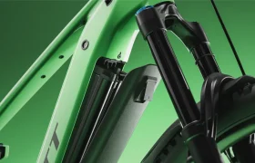 Primer plano de una bicicleta de montaña eléctrica SCOTT Strike 2027 de color verde en el que se aprecian el compartimento de la batería y la suspensión delantera sobre un fondo verde, destacando su comodidad y su potente motor Bosch CX.
