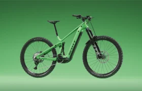 Bicicleta de montaña verde con suspensión total, neumáticos anchos, frenos de disco y el logotipo de «Scott», representada sobre un fondo verde con degradado. La SCOTT Strike 2027 ofrece una comodidad excepcional y viene equipada con el potente motor Bosch CX para una experiencia de conducción mejorada.