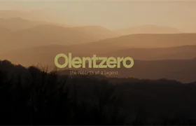Texto que reza «Olentzero: el renacimiento de una leyenda», centrado sobre un paisaje montañoso dorado y difuminado.