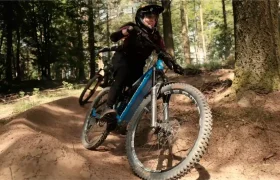 Un ciclista de montaña que va en una bicicleta azul por un sendero de tierra que atraviesa un bosque.