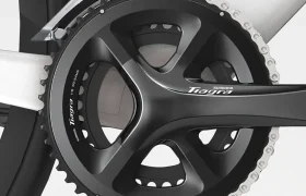 Primer plano de unas bielas y cadena Shimano Tiagra R4000 en un cuadro de bicicleta plateado, mostrando el desviador delantero y parte de la cubierta trasera.