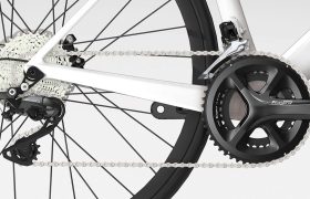 Primer plano del cambio trasero, la cadena, el casete y las bielas de una bicicleta, con componentes Shimano Tiagra R4000 en un cuadro blanco.