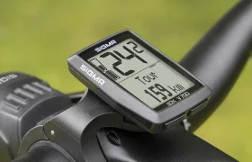 Primer plano de una computadora de bicicleta Sigma EOX VIEW 700 en un manillar, que muestra la velocidad y la distancia, con el fondo mostrando vegetación borrosa.