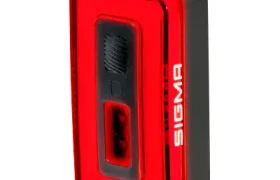 Luz trasera de bicicleta Sigma Nyte 70 rectangular roja y negra con cubierta translúcida y botón central, mostrada en ángulo sobre fondo blanco.