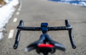 Primer plano del manillar de una bicicleta forrado con cinta Silca Nastro Cuscino y del sillín, con una carretera asfaltada al fondo. Se ve nieve a lo largo del borde de la carretera, lo que pone de relieve la necesidad de mayor comodidad y tacto durante los recorridos en días fríos.