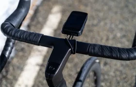 Primer plano del manillar de una bicicleta forrado con cinta Silca Nastro Cuscino negra, que ofrece un tacto y una comodidad excepcionales, con un ciclocomputador montado en una carretera al aire libre.