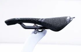 Vista lateral en primer plano de un sillín de bicicleta Prologo Scratch M5 PAS 3DMSS con una superficie negra perforada en forma de celosía montado sobre una tija de sillín blanca sobre un fondo liso.