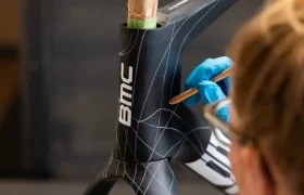 Una persona con guantes azules dibuja líneas de cuadrícula blancas en el cuadro de una bicicleta BMC VAR0 negra mate, con la horquilla y el tubo de dirección visibles.