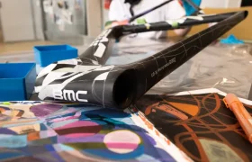 Una persona trabaja pintando un cuadro de bicicleta BMC VAR0 con diseños abstractos coloridos en un taller.